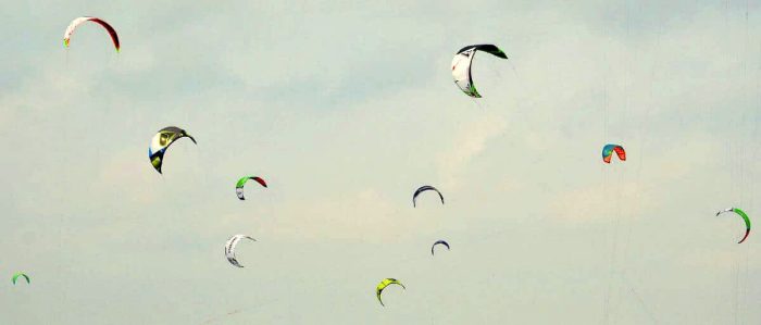Bunte Kite im Himmel, Windsurfen und Wassersportmöglichkeiten bei 2meere.de, entspannte Atmosphäre, windige Tage, Meeresrauschen, Freizeitaktivitäten an der Küste, Wassersport Event, Urlaub am Meer.