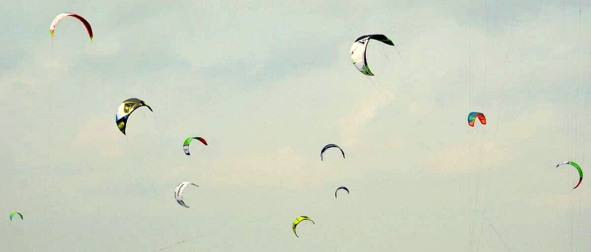 Bunte Kite im Himmel, Windsurfen und Wassersportmöglichkeiten bei 2meere.de, entspannte Atmosphäre, windige Tage, Meeresrauschen, Freizeitaktivitäten an der Küste, Wassersport Event, Urlaub am Meer.